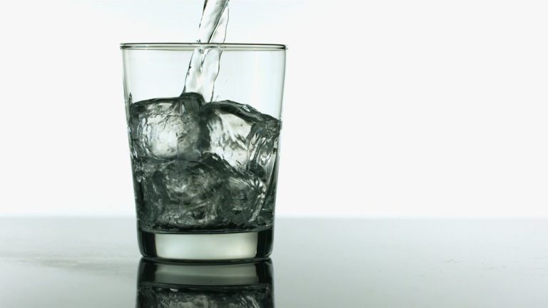 A glass full of ice with water being poured over it